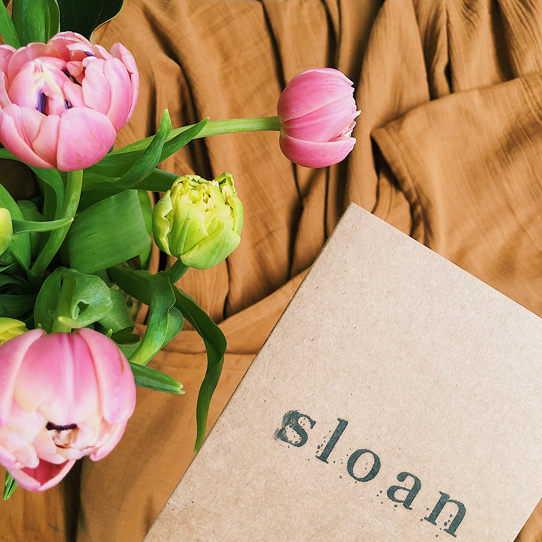 A flatlay of my Noelle dress, a card with Sloan stamped on it, and some fresh tulips.