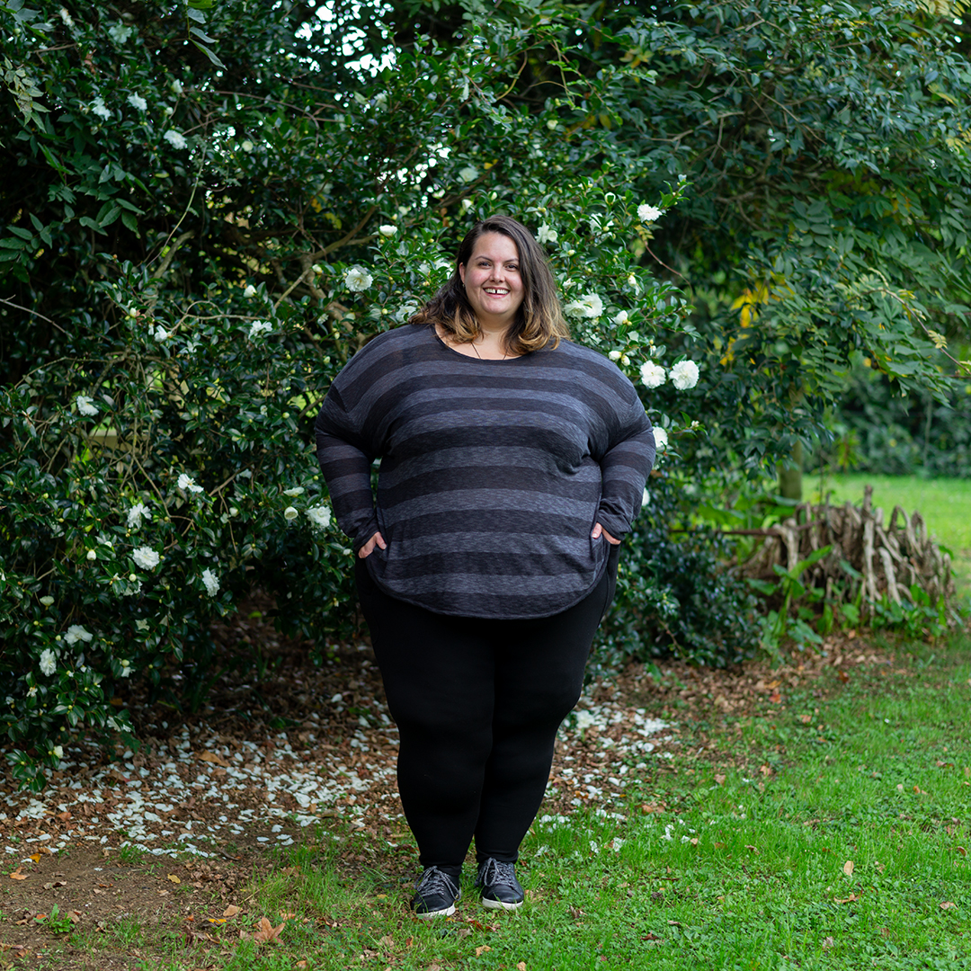 New Zealand plus size blogger Meagan Kerr is standing in a lush green garden in front of a camellia bush. She wears 17 Sundays Slub Knit Top in XL, Snag Tights Leggings in H and Ziera Shoes DANNI sneakers in 8