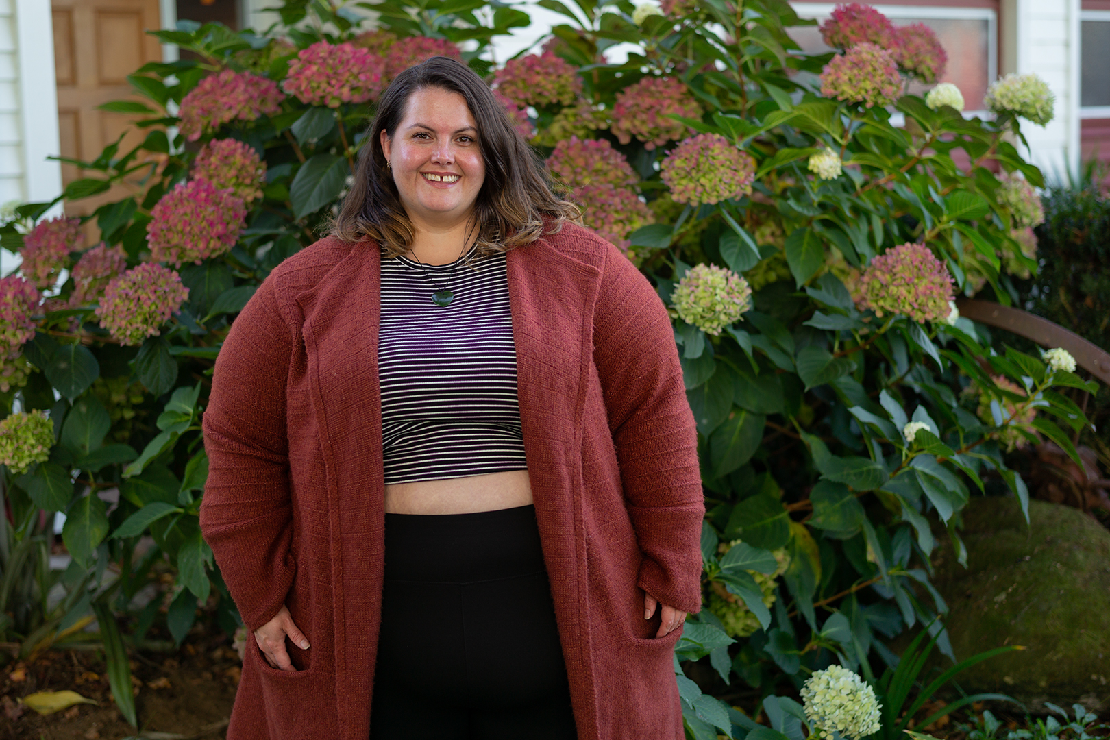 New Zealand plus size blogger Meagan Kerr stands in front of a hydrangrea bush. The photo shows her from her hips upward. Meagan wears a midriff baring City Chic Cheeky Stripe Top in XXL, Snag Tights Leggings in H, Old Navy Rust Cardigan in 4X