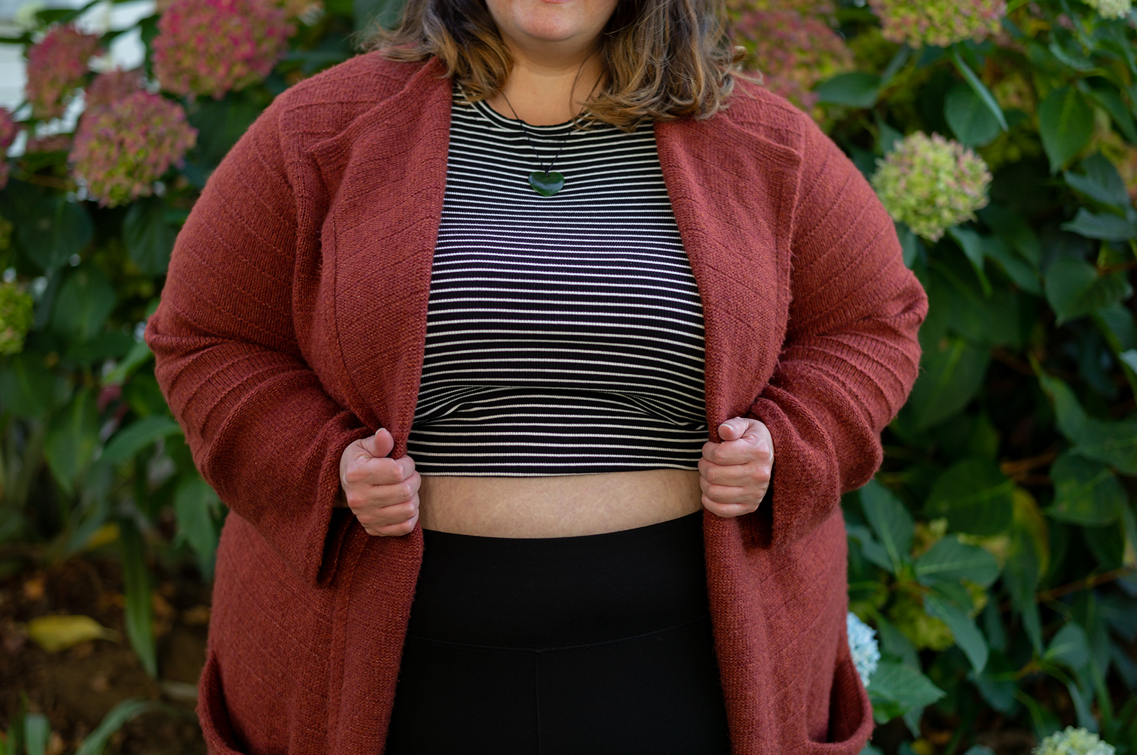 New Zealand plus size blogger Meagan Kerr stands in front of a hydrangrea bush. The photo is cropped to show from her chin to her hips. Meagan wears a midriff baring City Chic Cheeky Stripe Top in XXL, Snag Tights Leggings in H, Old Navy Rust Cardigan in 4X