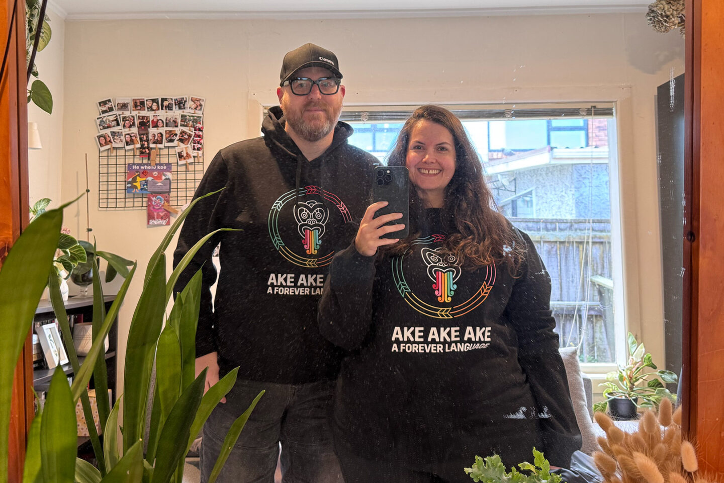 A mirror selfie of Meagan and Doug wearing Kia Kaha Te Reo Māori hoodies.